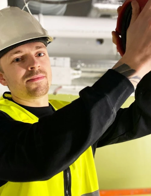Sprinklermontör i skyddsutrustning som arbetar med installation i takmiljö.