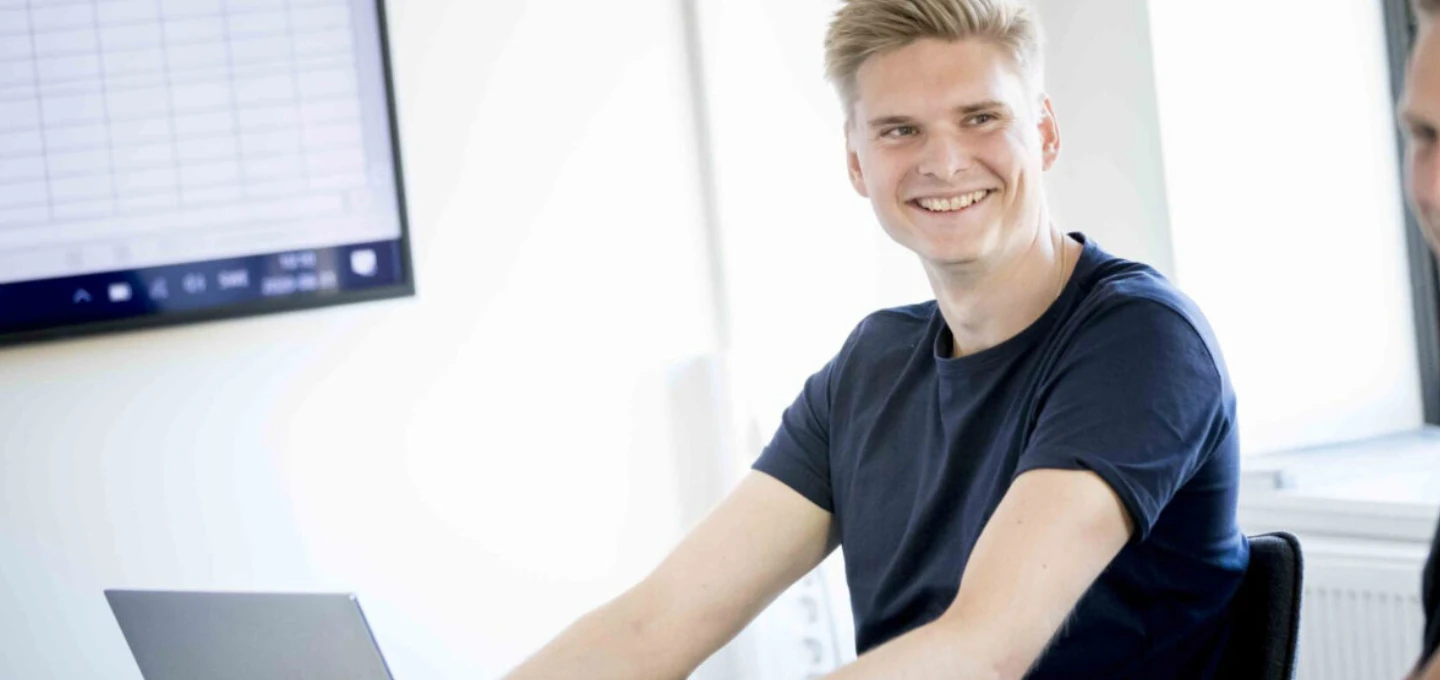 Medarbetare vid ett kontorsmöte med laptop och presentationsskärm.